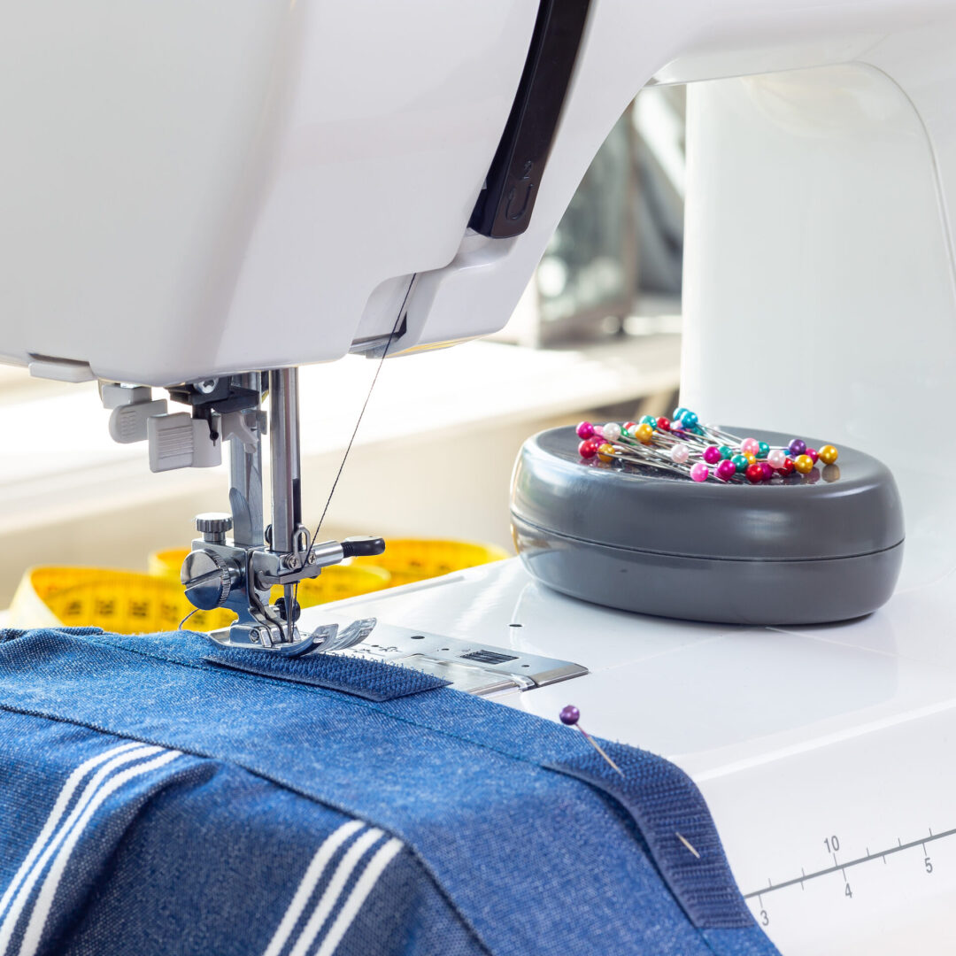 Sewing machine with striped blue white fabric and thread, pins on background, horizontal